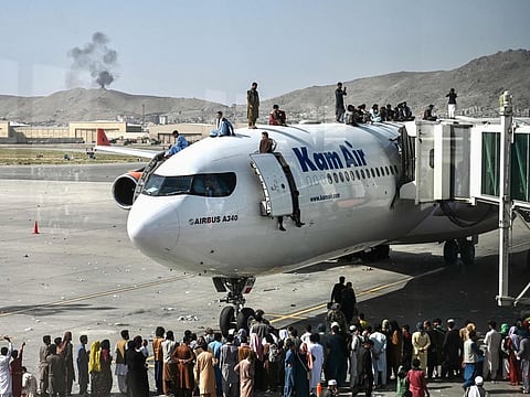 Afghan people climb atop a plane as they wait at the Kabul airport in Kabul on August 16, 2021, after a stunningly swift end to Afghanistan's 20-year war, as thousands of people mobbed the city's airport trying to flee the country.. 