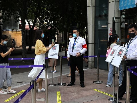 A woman shows her health status on a phone to a security guard, at an entrance to a shopping mall in Beijing, on August 23, 2021. 