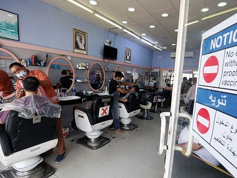 A notice is placed at the entrance to a barber shop in Kuwait City, prohibiting ustomers who are not vaccinated against the coronavirus from entering, on September 3, 2021.