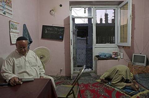 In this photo taken on August 29, 2009, Zebulon Simentov, the last known Jew living in Afghanistan, sits at his dining room table during Shabbat in his Kabul home, as Shirgul Amiri, right, a local Muslim friend, prays.
