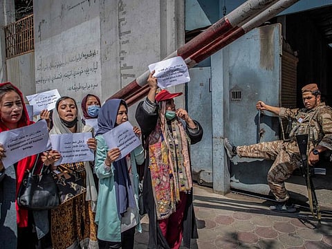 A Taliban member watches as Afghan women hold placards during a demonstration demanding better rights for women in front of the former Ministry of Women Affairs in Kabul on September 19, 2021. 