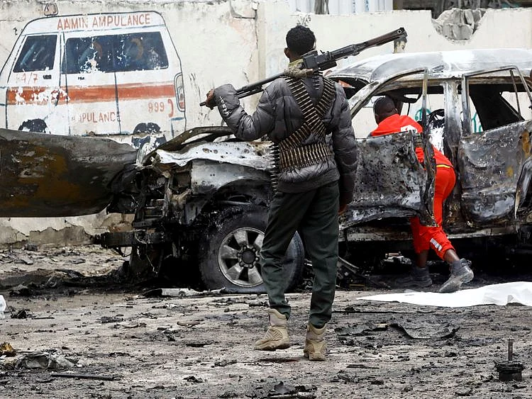 A police officer keeps watch as Red Crescent workers remove the body of a victim at the scene of a suicide car bomb explosion near the president's residence, in Mogadishu, Somalia, September 25, 2021. 