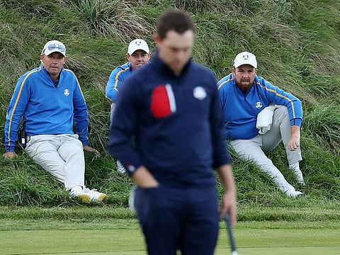 Captain Padraig Harrington of Team Europe, Rory McIlroy and Shane Lowry look on as Patrick Cantlay of Team US putts on the 18th green 