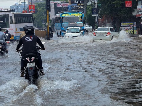 Commuters wade through a waterlogged road during heavy rain in Kozhikode on October 12, 2021. 
