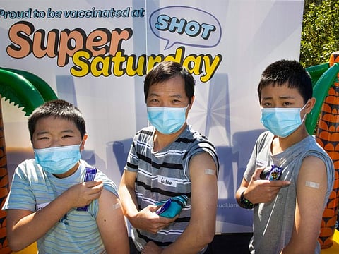 Johnson, left, Bailou and Benson, right, Su of Auckland show their bandaids after receiving their vaccination in Auckland on October 16, 2021. 
