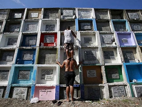 File photo: A man stands on the shoulders of a friend to reach and repaint the tomb of his departed relative buried in an 'apartment-style' grave inside a cemetery in Navotas city, north of Manila.