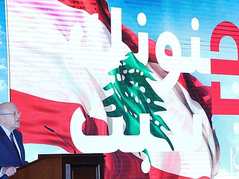 Lebanese Prime Minister Najib Mikati speaks as he stands near a slogan that reads 'We love you in your madness' displayed on a screen at the government palace in Beirut on November 4, 2021. 