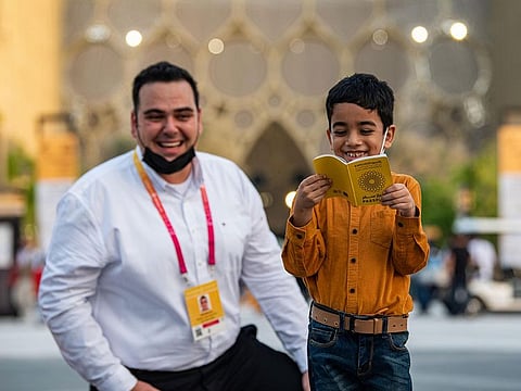 Hasan flips through his replacement Expo 2020 Dubai passport presented by Expo staff member Fabio (left)