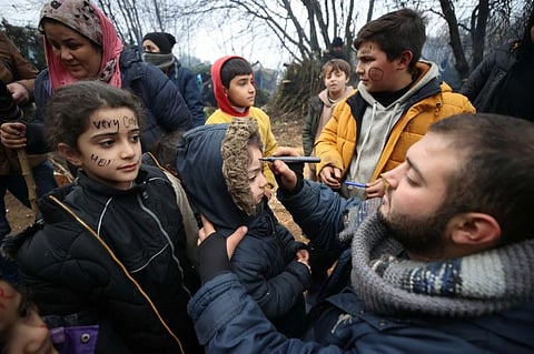 A man writes words on children's faces in front of journalists in a makeshift camp on the Belarusian-Polish border in the Grodno region, Belarus, on November 12, 2021. 