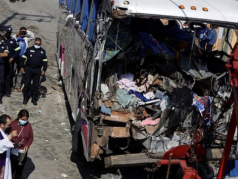 A priest blesses the bus at the scene where at least 19 people were killed and 20 more injured after a passenger bus traveling on a highway crashed into a house, according to authorities, in San Jose El Guarda, on November 26, 2021.  