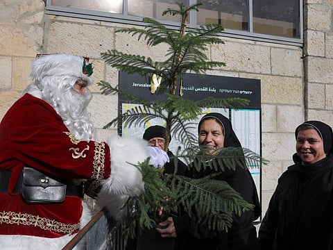 Eisa Kassissieh, dressed as Santa Claus, gives away a Christmas tree to nuns in Jerusalem's Old City on December 23, 2021. 