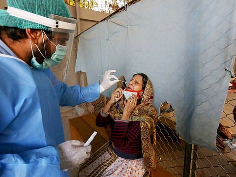 A health care worker takes a nasal swab sample from a woman at a COVID-19 testing facility at a hospital in Karachi, Pakistan.