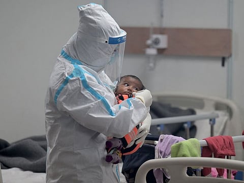 A health worker wearing a Personal Protective Equipment (PPE) suit comforts a child infected with COVID-19 coronavirus inside a ward at the Commonwealth games (CWG) village sports complex, temporarily converted into a COVID-19 coronavirus care centre, in New Delhi on January 5, 2022.