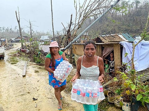 In this photo taken on January 5, 2022, residents carry bottled water given as aid from a non-governmental organisation in Burgos town, Siargao island, weeks after super Typhoon Rai devastated the island. 