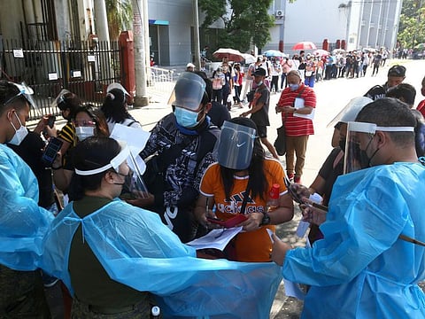 Health workers check identification documents of people queueing up for swab tests outside a gymnasium in Manila on January 7, 2022, as infections driven by the Omicron variant have tripled in the last two days in the nation's capital. 