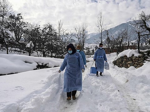 Health workers walk on a snow covered road during a door to door vaccination drive in Khag village in the Budgam district, some 55km from Srinagar.