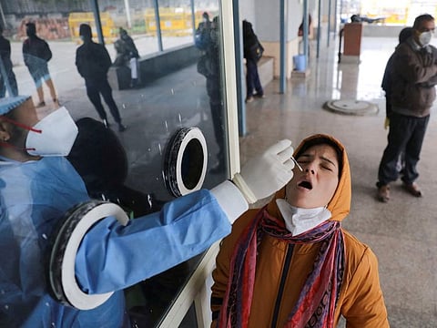 A healthcare worker collects a test swab sample from a woman inside a hospital in New Delhi.