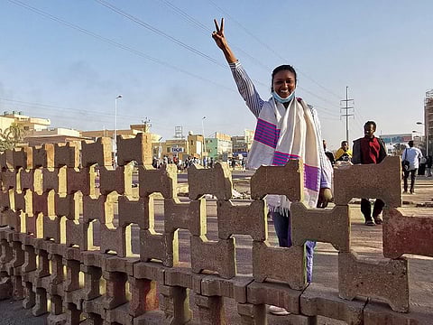 A woman flashes the victory sign standing behind a barricade as demonstrators attend a protest in Khartoum, Sudan, January 20, 2022. 