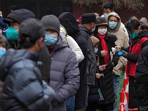 A volunteer wearing a face mask to help protect from the coronavirus checks the name list as residents line up during a mass coronavirus testing at a school in Fengtai District in Beijing, Monday, Jan. 24, 2022. Chinese authorities have lifted a monthlong lockdown of Xi'an and its 13 million residents as infections subside ahead of the Winter Olympics.