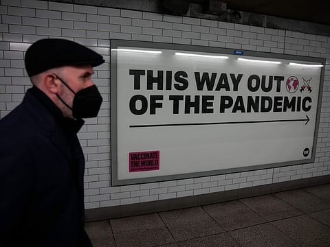 A man wearing a face mask to curb the spread of coronavirus walks past a health campaign poster from the One NGO, in an underpass leading to Westminster underground train station, in London, Thursday, Jan. 27, 2022.