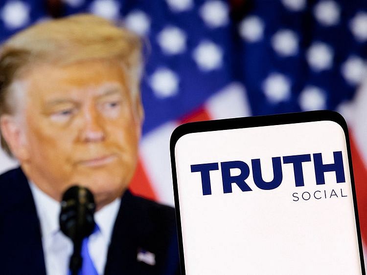 The Truth social network logo is seen on a smartphone in front of a display of former U.S. President Donald Trump
