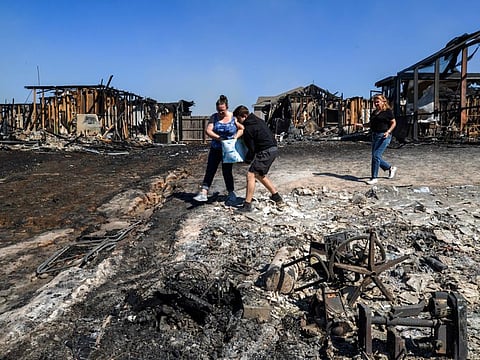Residents pour water on hotspots behind homes in Panama City Saturday, March 5, 2022 after a wildfire that started Friday. The three neighbours were taking water out of the pool from one of the burned out homes to use on the hotspots.