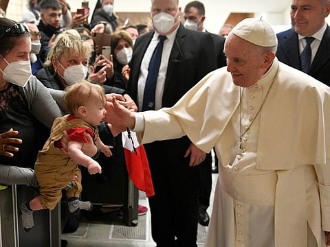 Pope Francis touches the head of a baby as he greets people at the weekly general audience at the Paul VI Hall at the Vatican, March 16, 2022. 