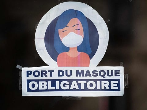 This photograph taken on March 13, 2022, shows a sticker reading "The wearing of a mask is mandatory" on the door of a store in Paris.