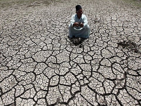 An Egyptian farmer squats down on cracked soil to show the dryness of the land due to drought in a farm formerly irrigated by the river Nile, in Al-Dakahlya