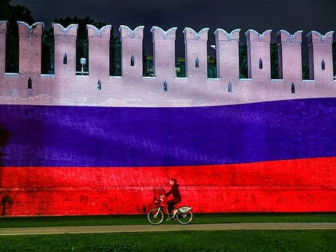File photo: A woman rides a bicycle past a part of the Kremlin wall where the Russian national flag is projected, in Moscow. 