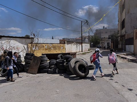 Palestinian students walk past piles of tires that are collected and prepared to be set on fire during possible future Israeli army incursions, in the West Bank refugee camp of Jenin.