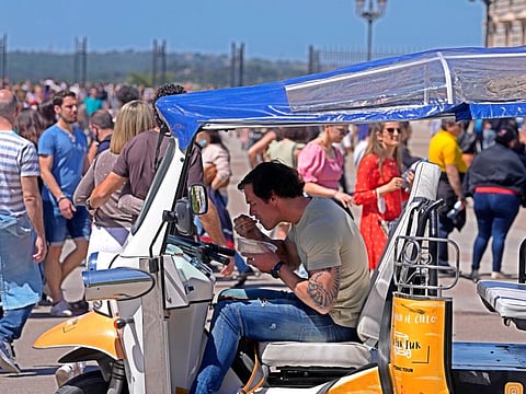 A Tuk-Tuk driver grabs something to eat while waiting for tourists outside the Royal Palace in Madrid, on April 16, 2022. 