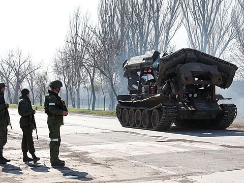 Service members of pro-Russian troops stand next to a combat engineering vehicle, as evacuees board buses to leave the city during Ukraine-Russia conflict in the southern port of Mariupol on April 20, 2022.  