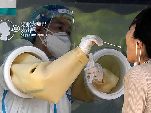 A worker takes a swab sample at a COVID test center on Tuesday, April 26, 2022, in Beijing.