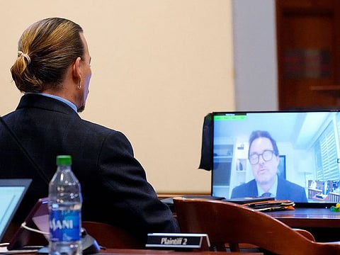 Actor Johnny Depp listens as Jack Whigham, talent manager for Depp, is seen on a monitor as he testifies remotely at Fairfax County Circuit Court during Depp's defamation case against ex-wife, actor Amber Heard, in Fairfax, Virginia, U.S., May 2, 2022. 