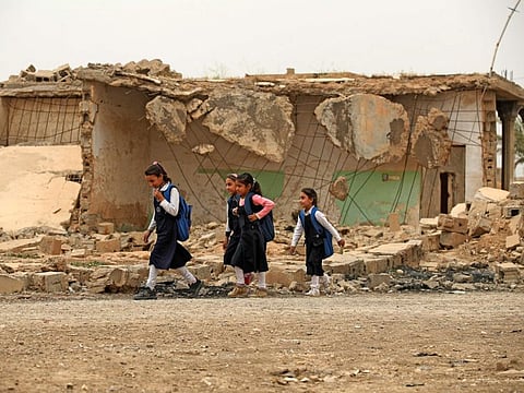 Iraqi pupils walk past a destroyed house in the war-ravaged village of Habash, some 180 kilometres north of the capital Baghdad, on April 25, 2022. 