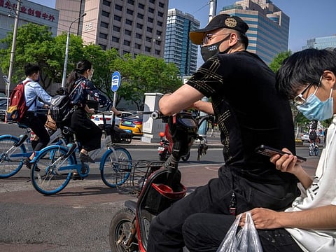 Commuters wearing face masks wait at an intersection in the central business district in Beijing, Thursday, May 5, 2022.