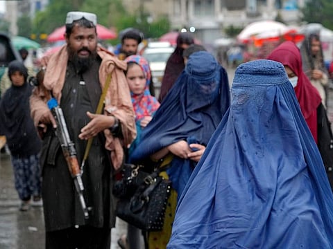 Women walk through the old market as a Taliban fighter stands guard in Kabul.