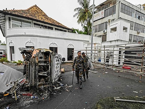 Security personnel walk past a burned vehicle near Sri Lanka's former prime minister Mahinda Rajapaksa's official residence 'Temple Trees', a day after they were torched by protesters in Colombo on May 10, 2022. 