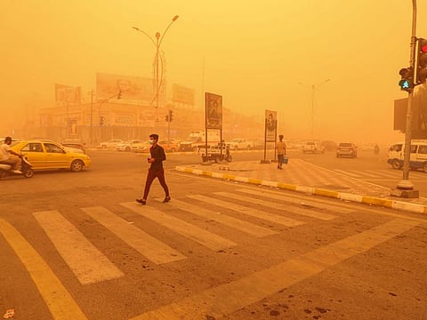 A pedestrian crosses a road in the city of Nasiriyah in Iraq's southern Dhi Qar province on May 16, 2022 amidst a heavy dust storm.