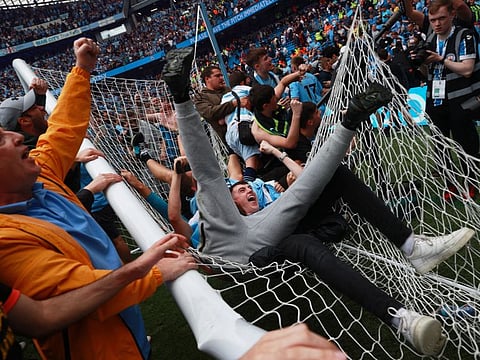 Manchester City fans celebrate on the pitch after winning the Premier League. 