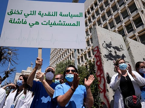 A nurse holds an Arabic placard that reads: "Monetary policy that stifles hospitals is a failure," as he protests with other medical workers and doctors the deteriorating economic conditions, outside the Central Bank, in Beirut, Lebanon, on May 26, 2022. 