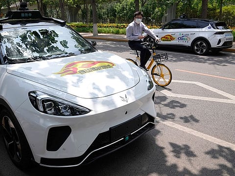 A man on a bicycle rides past self-driving taxis developed by tech giant Baidu Inc. on June 14, 2022, in Beijing.