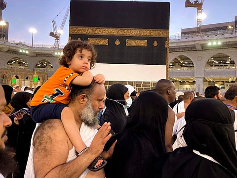 A Muslim pilgrim carries his son as he circumambulates around the Kaaba at the Grand Mosque in Mecca on July 5, 2022.  