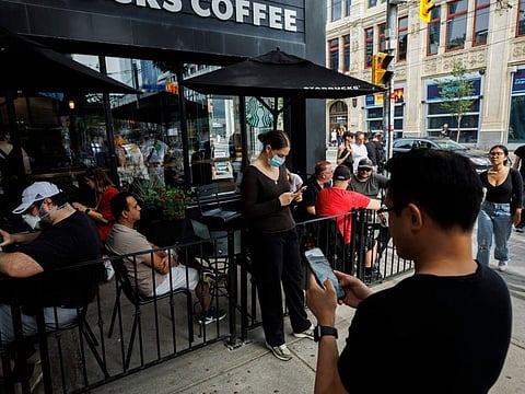 People use electronics outside a coffee shop in Toronto amid a nationwide Rogers outage, affecting many of the telecommunication company's services, Friday, July 8, 2022.