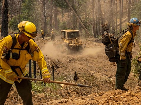 A bulldozer passes firefighters cutting vegetation to broaden a fireline at the Oak Fire near Mariposa, California, on July 25, 2022.