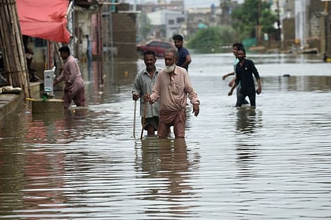 Residents wade across a flooded street after heavy monsoon rains in Karachi on July 26, 2022. 