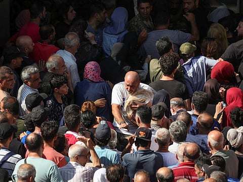 A man holds stacks of bread as he makes his way through a crowd of people queuing for bread outside a bakery in Beirut, Lebanon July 27, 2022.