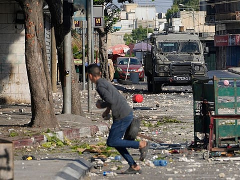 A Palestinian demonstrator throws stones as the Israeli army carries out an operation in the West Bank town of Nablus, on August 9, 2022. 