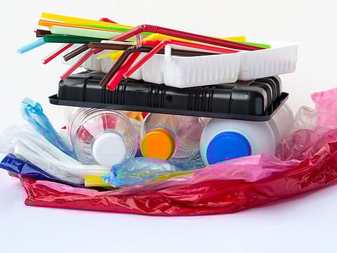 A pile of single use plastic garbage including  water bottles, drinking straws, food packages and carrier bags on white background with copy space. Pollution concept.